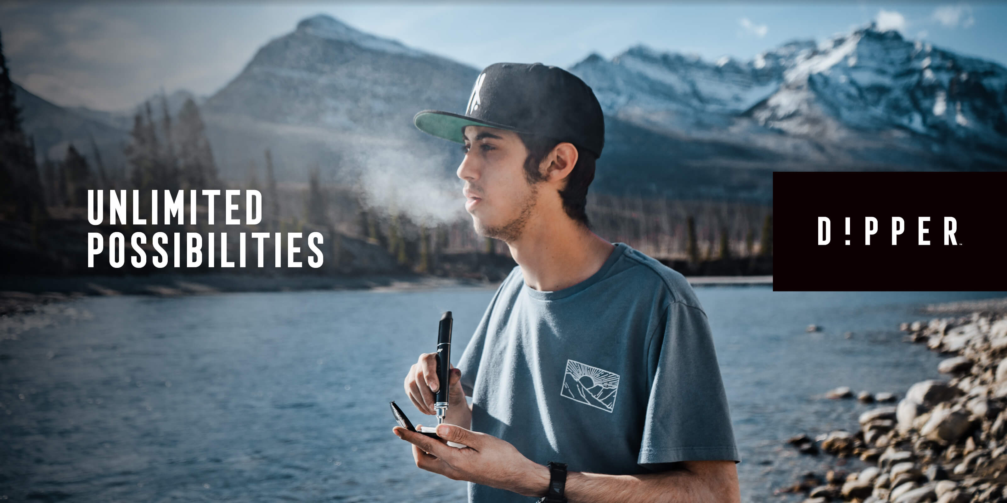 model with dipper dab pen vaping outdoors with mountains and a river behind them