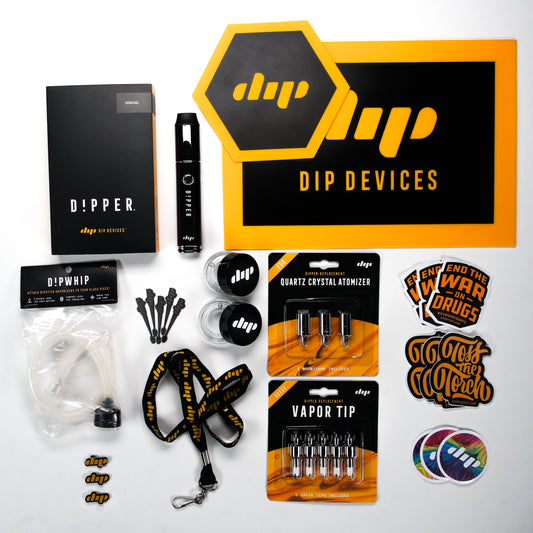 Dip Devices starter bundle featuring a Charcoal Dipper electric dab pen, 5 Vapor Tip Atomizers, 3 Quartz Crystal Atomizers, a DipWhip, 2 dab mats, 2 glass Dip containers, 2 lapel pins, assorted stickers, and 5 dab tools.
